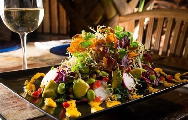 large superfood salad on a dark rectangle plate sitting next to a glass of white wine in aruba