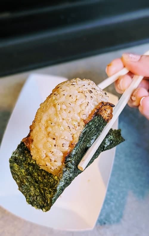 vegan rice japanese onigiri held with chop stick over a white paper tray in portland