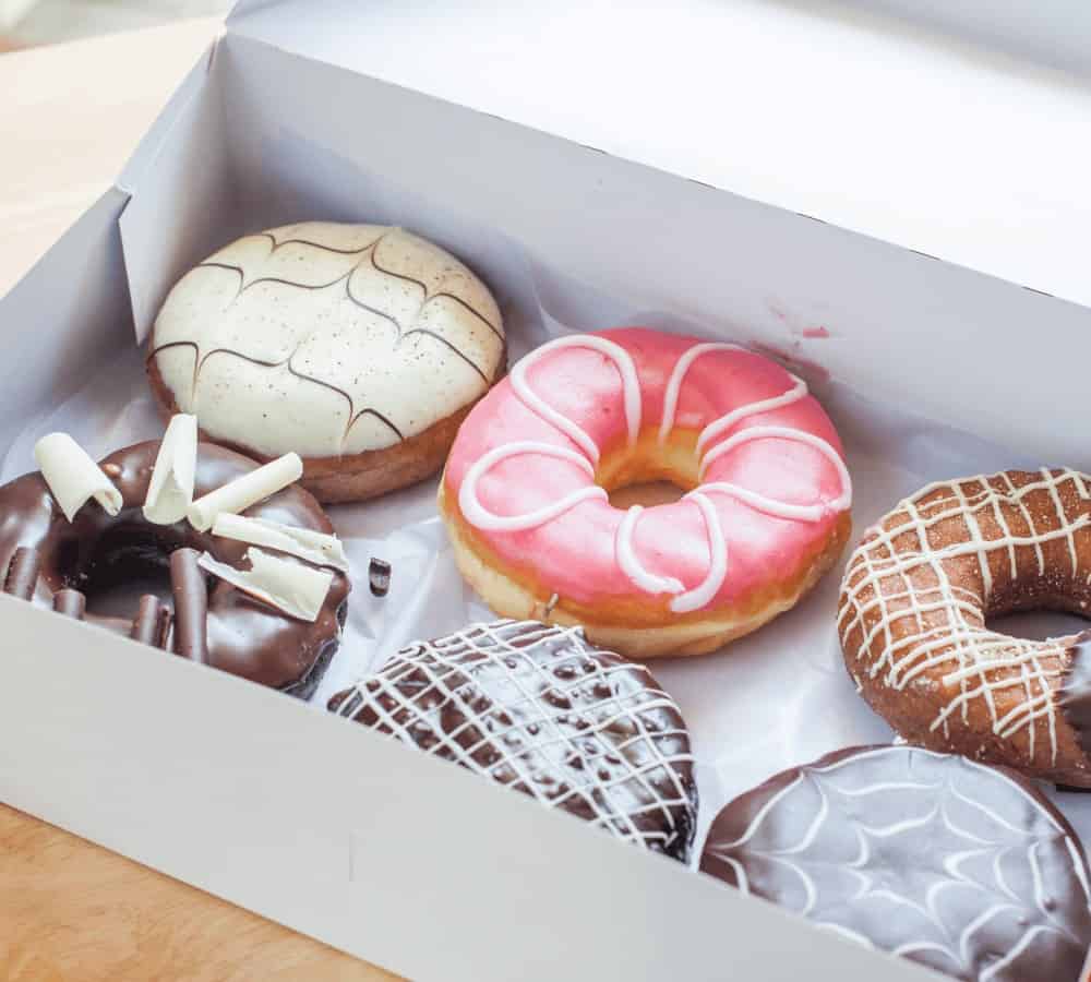 a white box filled with six different donuts covered in pink icing, white icing, and chocolate