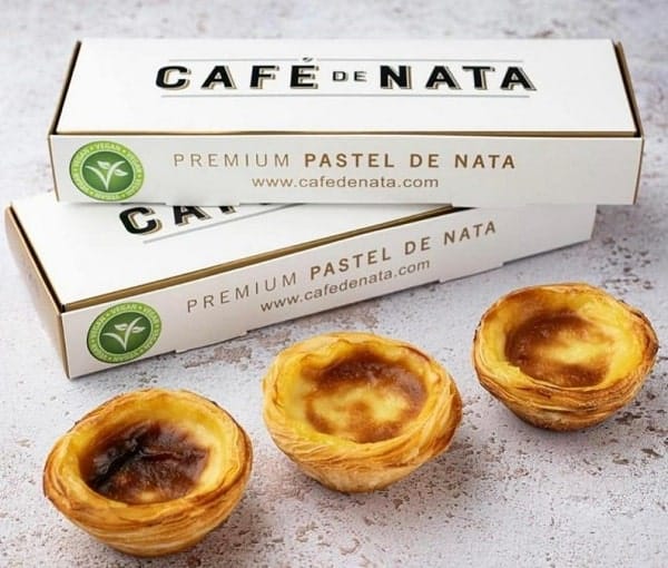 three vegan custard tarts in front of two white boxes with green vegan stickers from cafe de nata in london