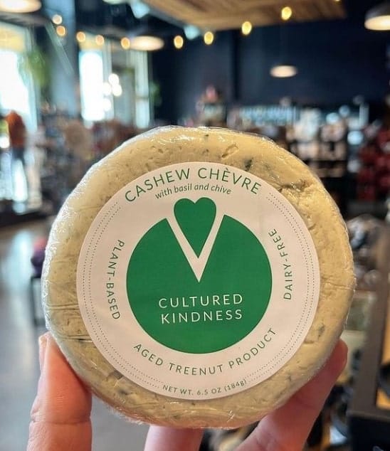 round vegan goat cheese wheel held with one hand in the middle of the store