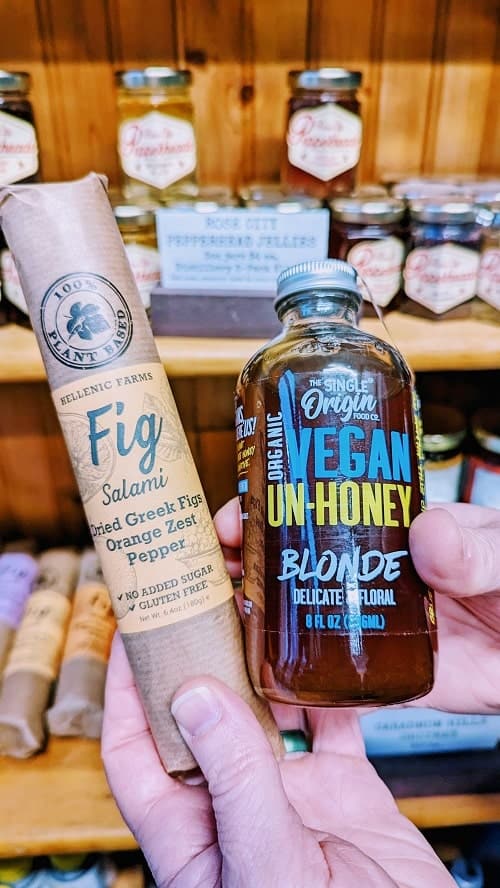 a brown bottle of vegan honey held next to a round tube of vegan fig salami at cultured kindness in portland