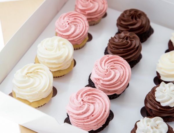 a white box filled with rows of vanilla and chocolate cupcakes topped with pink, white, and chocolate buttercream