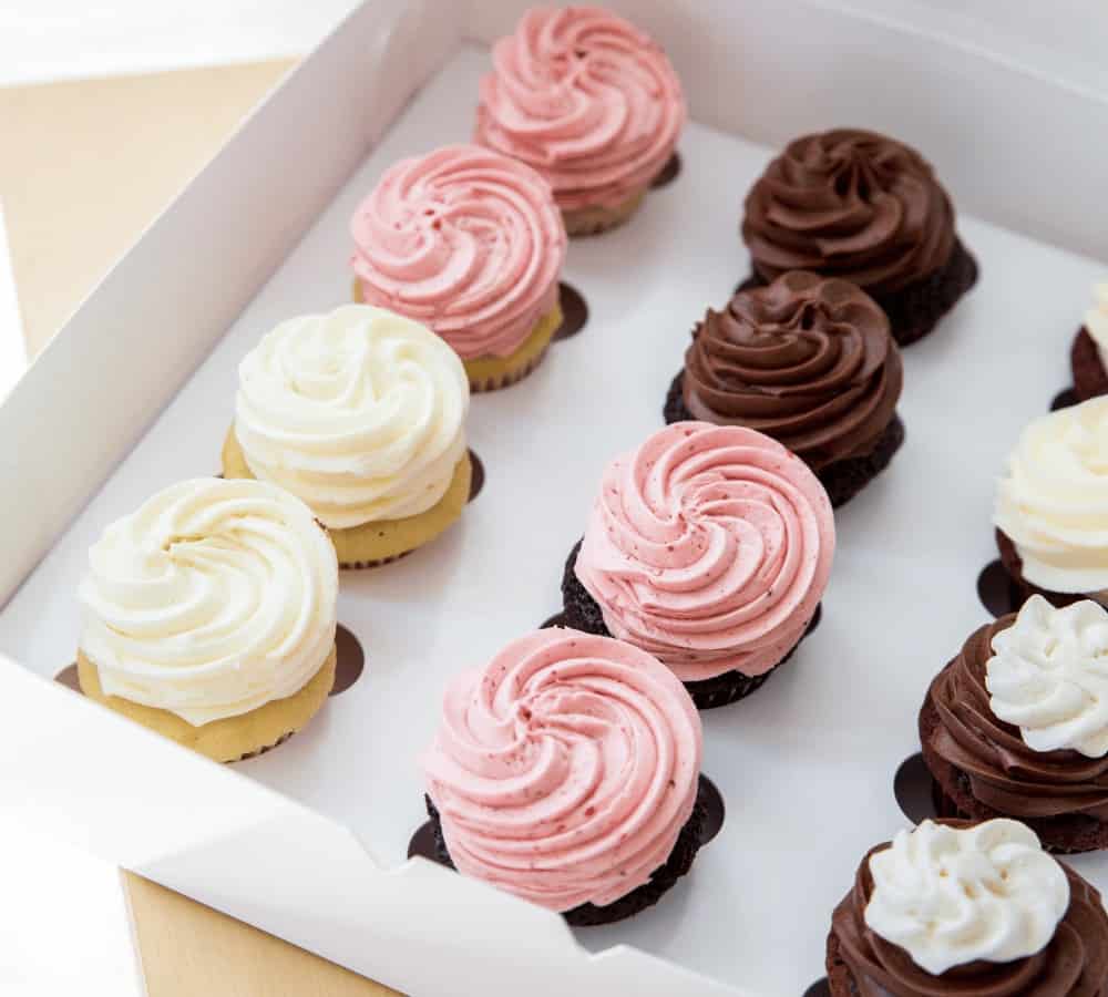 a white box filled with rows of vanilla and chocolate cupcakes topped with pink, white, and chocolate buttercream