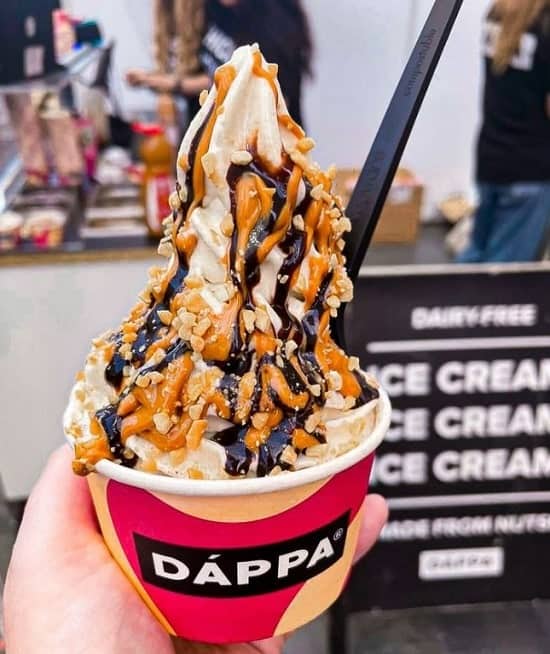 a cup of vegan soft serve ice cream topped with a chocolate drizzle and a sprinkle of chopped nuts at dappa in london