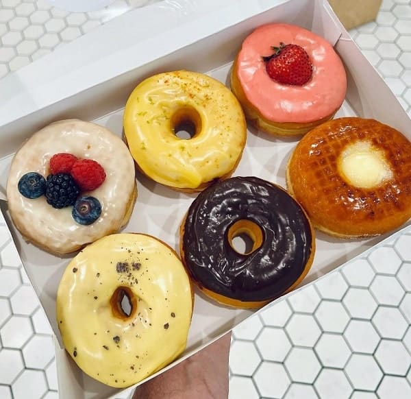 a white box filled with six vegan donuts topped with pink and yellow icing, chocolate and bruleed sugar at donut friend in LA