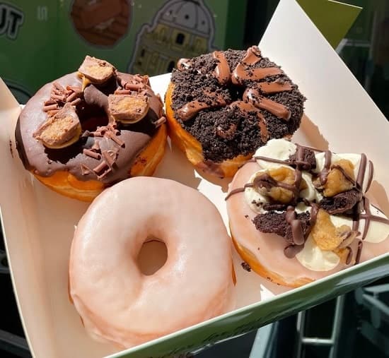 a box of four vegan donuts topped with vanilla icing, chocolate icing, cookies, and cookie dough from doughnut time in london