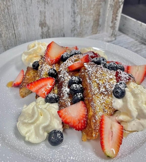 a plate of golden vegan french toast covered in whipped cream, strawberries and blueberries from innocent yesterday  in nyc