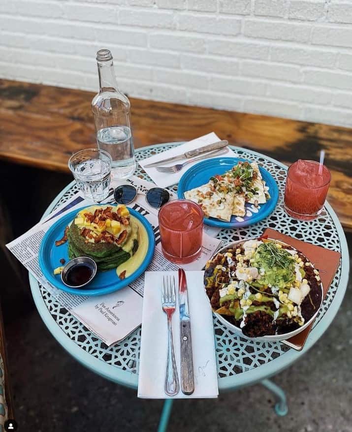 a colorful tile table with three vegan brunch dishes next to a pink cocktail and a bottle of water at jajaja nyc