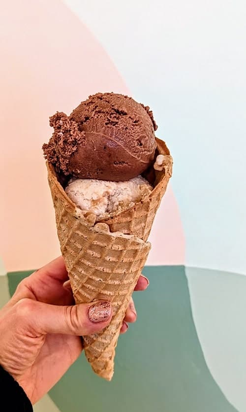 vegan and gluten free waffle cone with one scoop of chocolate and a second scoop of peanut butter ice cream in front of a pink and green wall in portland