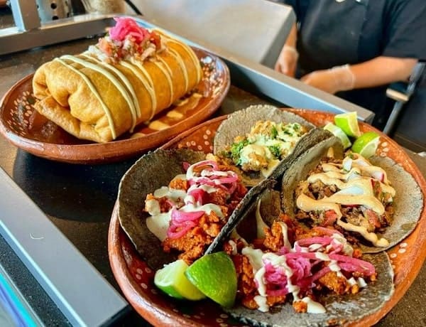 a plate of four colorful vegan tacos next to a giant stuffed vegan burrito covered in sour cream at mis tacones in portland