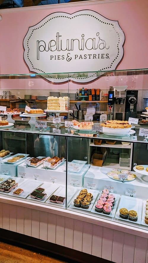 the clear glass dessert case at petunias pastries and pie with their logo on a pink background behind it
