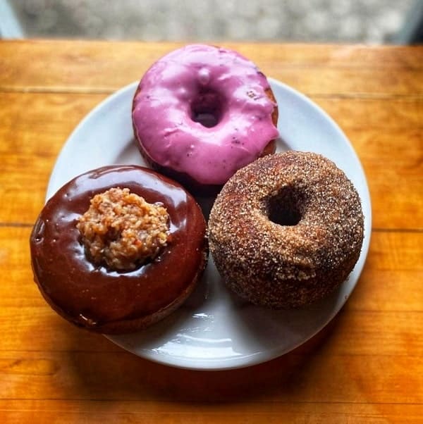 three vegan donuts on a white plate one with pink icing, one with dark chocolate and the other with cinnamon and sugar in portland