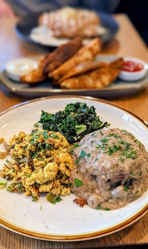 vegan biscuit covered in mushroom gravy next to steamed greens and tofu scramble on a white plate in portland