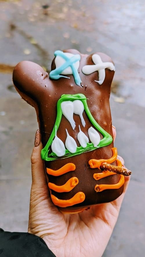 vegan voodoo doll shaped donut covered in dark chocolate frosting with a pretzel stake sticking out in portland