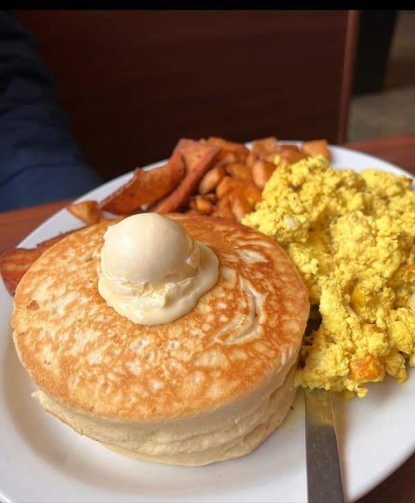 one large golden vegan pancake topped with a round dollop of butter next to fluffy scramble tofu on a white plate at cycle dogs in seattle