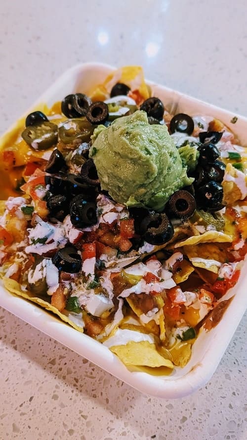 white square dish filled with vegan nachos topped with guac, olives, salsa, and cheese at el borracho in seattle