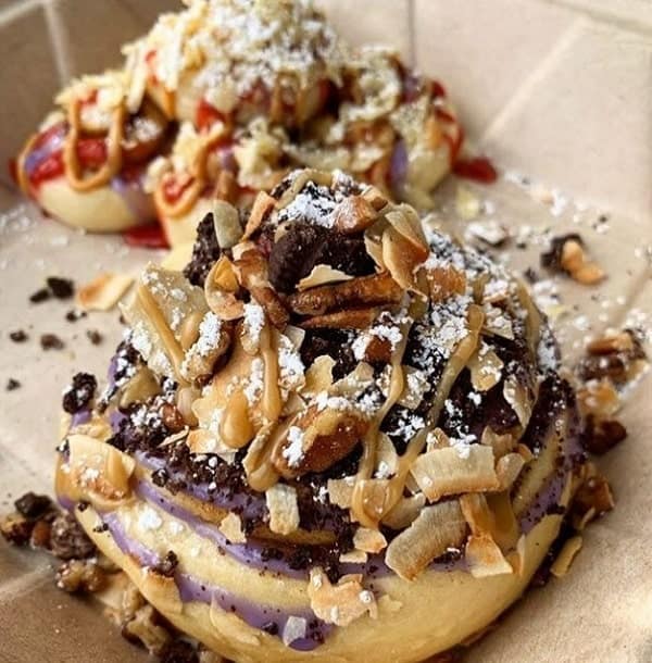 a large vegan cinnamon roll topped with cookie pieces, nuts and caramel sauce in portland