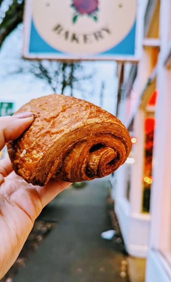 one golden vegan croissant held in front of the lazy cow bakery sign in seattle