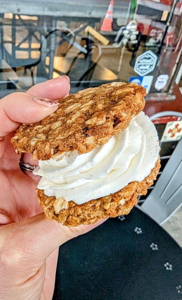 one vegan and gluten free oatmeal cookie sandwich with a thick layer of white butter cream in the center held in front of the nuflours bakery in seattle