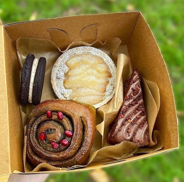 a large brown square pastry box filled with a vegan cinnamon rollm tart, a chocolate cookie, and more in portland