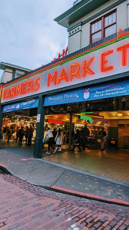 the neon red lettered entrance to the pike place market on an overcast day in seattle