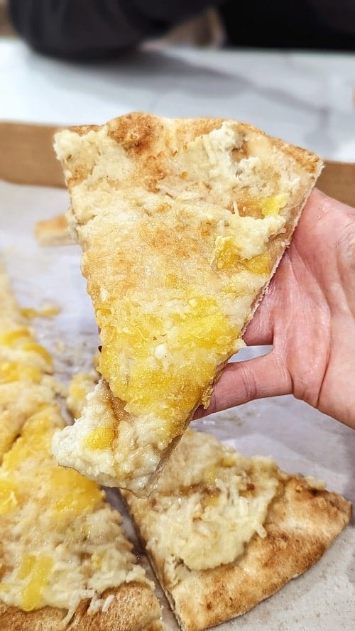 a slice of vegan cheese pizza held with one hand at plantiful superfoods in seattle