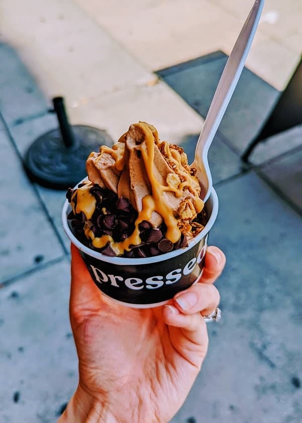 bowl of vegan chocolate ice cream topped with peanut butter sauce, chocolate chips, and granola held above a side walk in washington dc