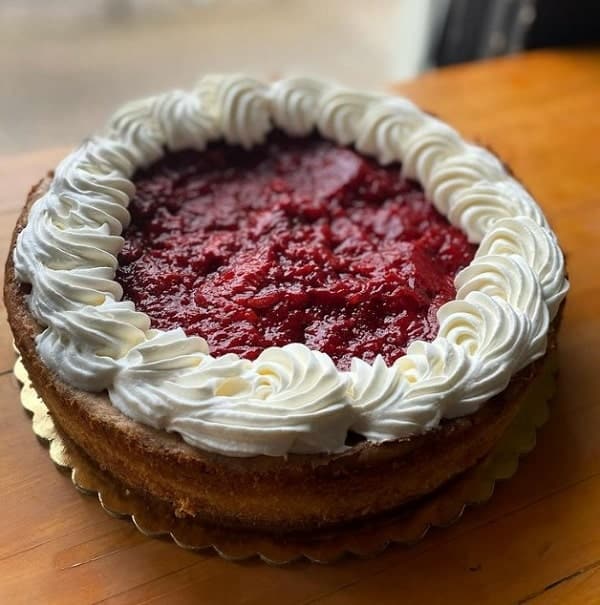large round vegan cheese cake topped with cherries and outlined in white swirled buttercream on the top edge in portland