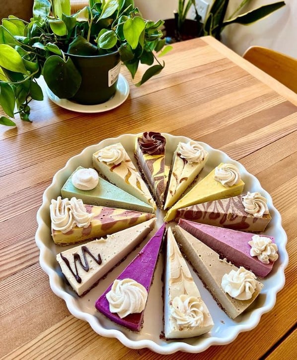 a white round plate filled with 12 slices of colorful vegan cheese cake slices neatly arranged in portland