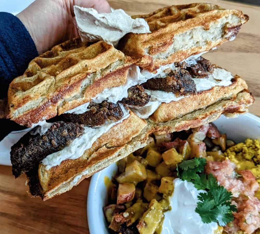 vegan waffle sandwich with sausage and cream in the middle held over a mexican breakfast bowl at cafe nectar in portland
