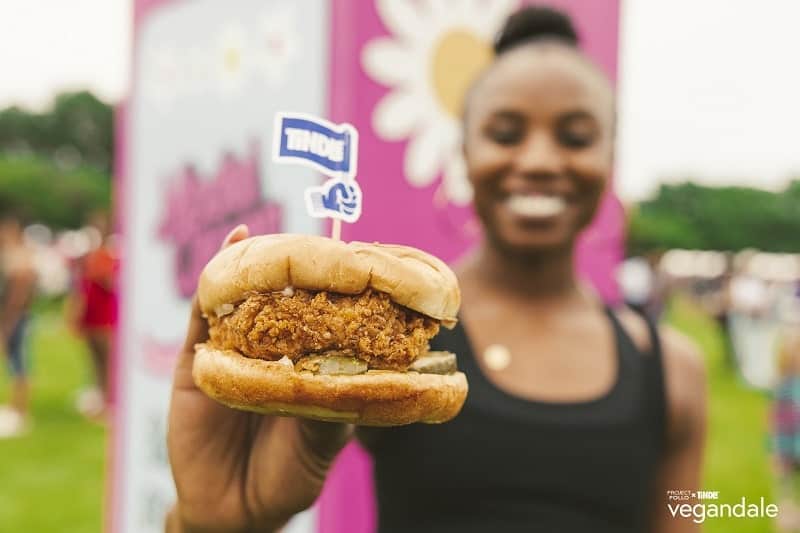 vegan fried chicken sandwich held by a women in front of a pink background with white daisies at the vegandale festivale