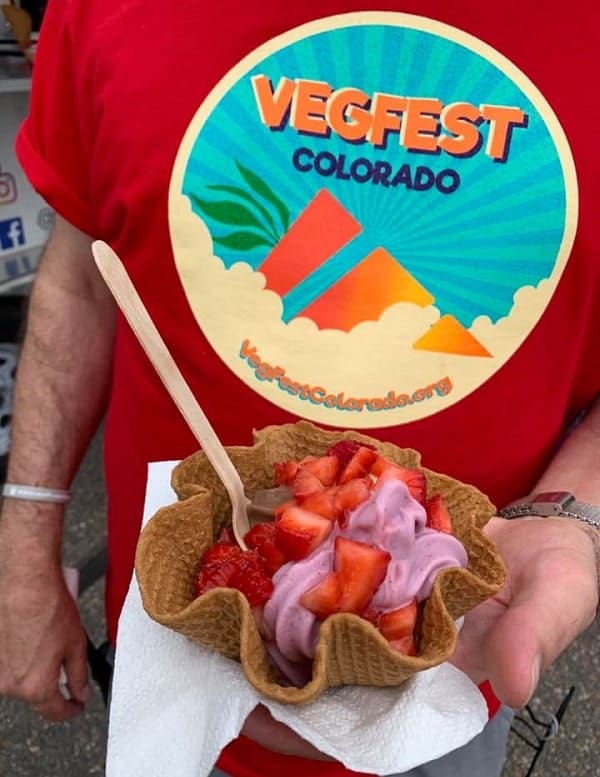 a person holding a waffle cone with vegan ice cream while wearing a red tshirt that says vegfest colorado