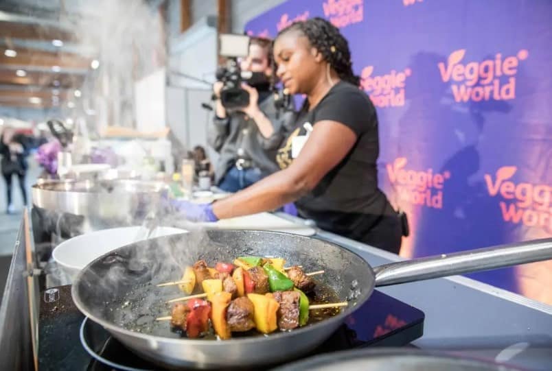 a women giving a vegan cooking demo with a hot pan steaming with veggies at veggie world expo