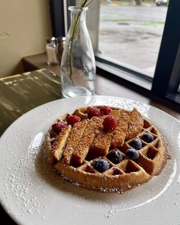one large golden vegan waffle on a round white plate topped with crispy fried vegan chicken at wayward vegan in seattle