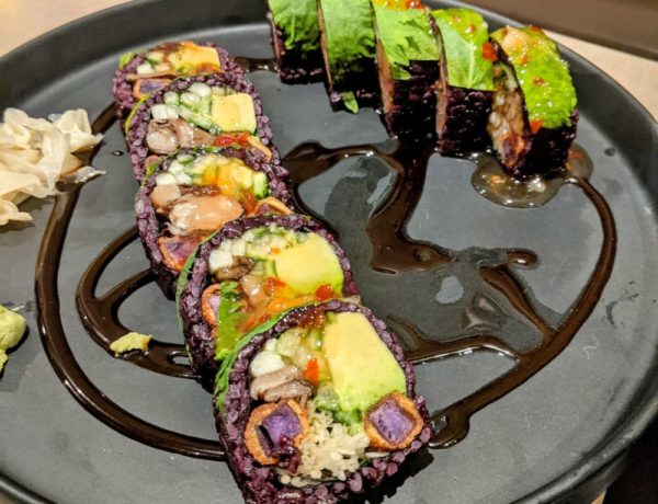 vegan sushi rolls with purple rice and covered with avocado on a black plate at beyond sushi in nyc