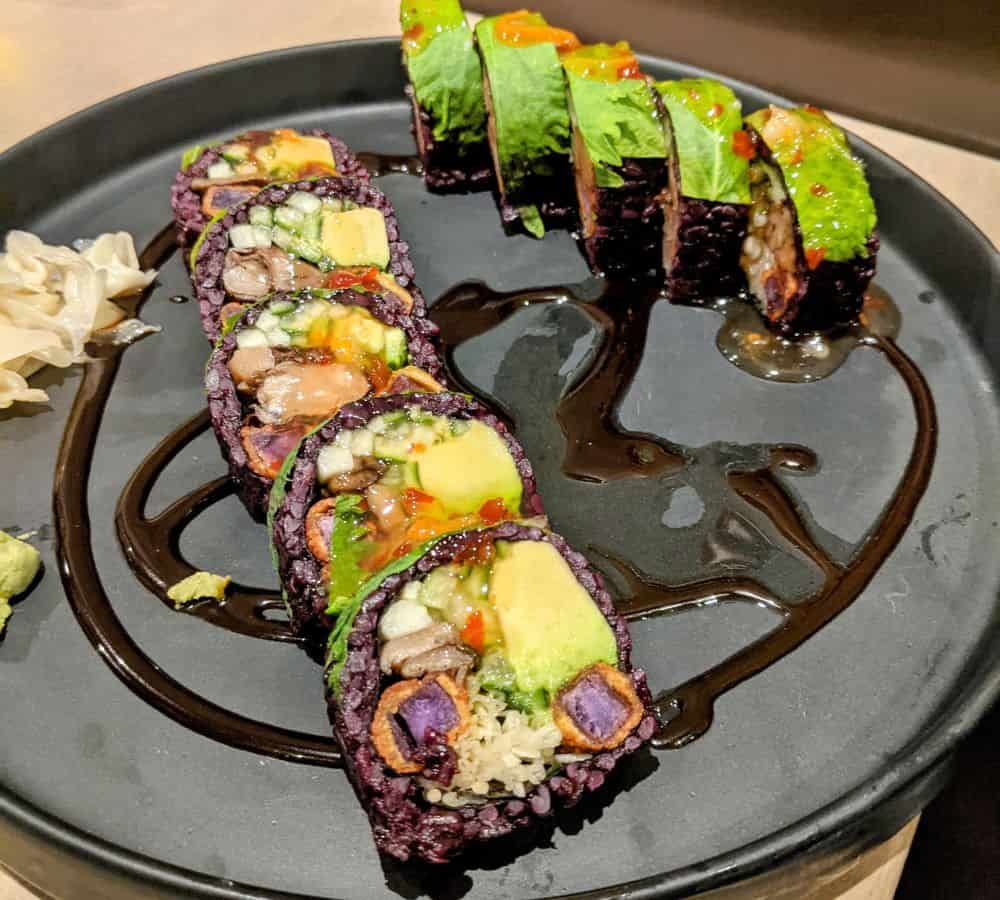 vegan sushi rolls with purple rice and covered with avocado on a black plate at beyond sushi in nyc