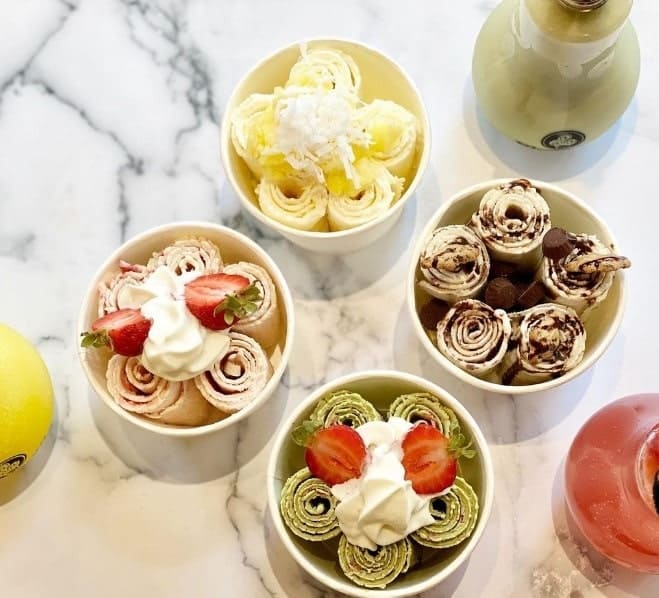 four white bowls filled with vegan ice cream rolls and topped with a mix of sliced fruit and chocolate from blossom ice cream in NYC