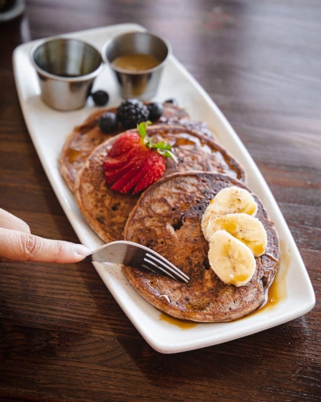 a stack of three golden vegan pancakes on a long white rectangle plate topped with banana and strawberry slices at citizen eatery in austin