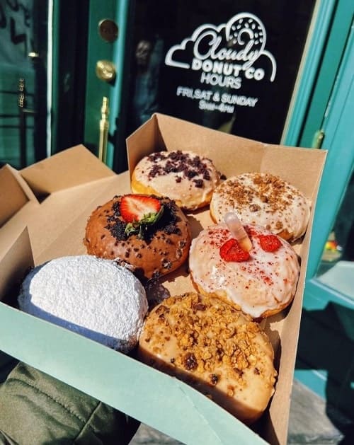 a box of six vegan donuts topped with chocolate, cookie crumbs, nuts and powdered sugar from the vegan bakery cloudy donut in NYC