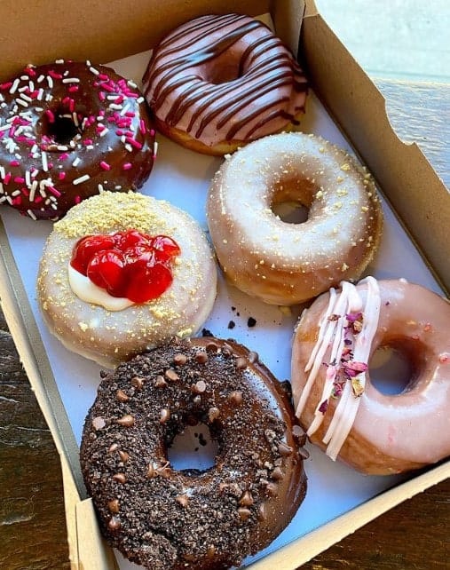 a box of six colorful vegan donuts topped with glaze, chocolate, pink icing and sprinkles from dun well donuts in NYC