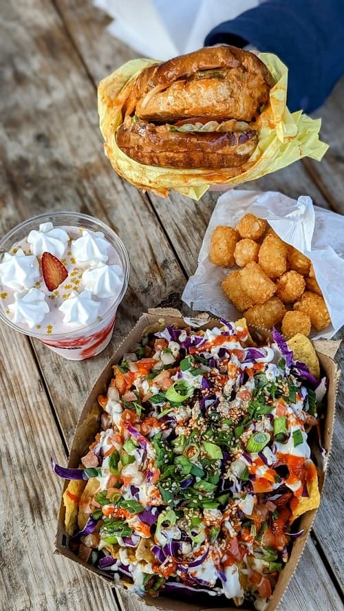 spread of vegan bbq korean nachos, chicken burger, tater tots and a strawberry milkshake at the vegan nom food truck park
