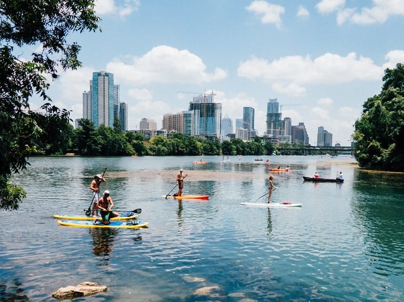 people kayaking and stand up paddle boarding on lady bird lake on a sunny day in austin