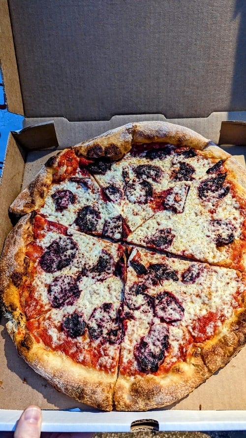 large round vegan pizza covered in cheese and dark pepperoni made from beets in a cardboard box in austin