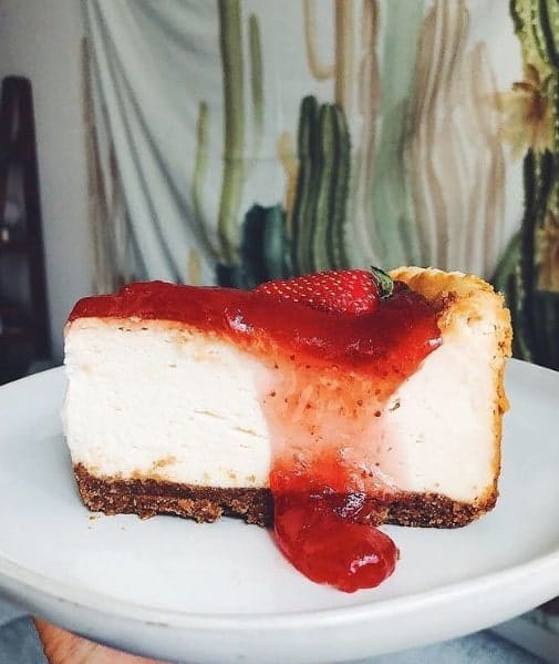 a slice of vegan cheese cake with a graham cracker crust and topped with fresh strawberries from peacefood cafe in NYC