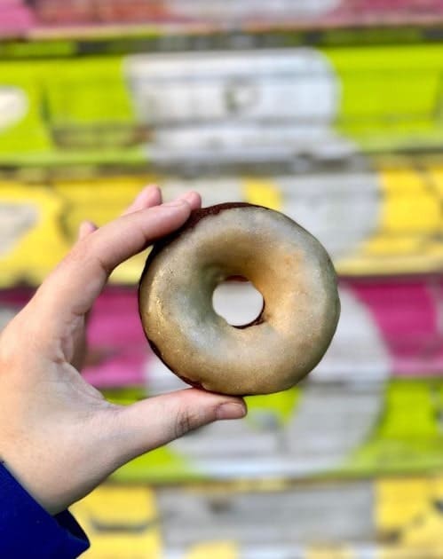 a vegan glazed chocolate planet bake donut held in front of a lime, green, and pink mural in NYC