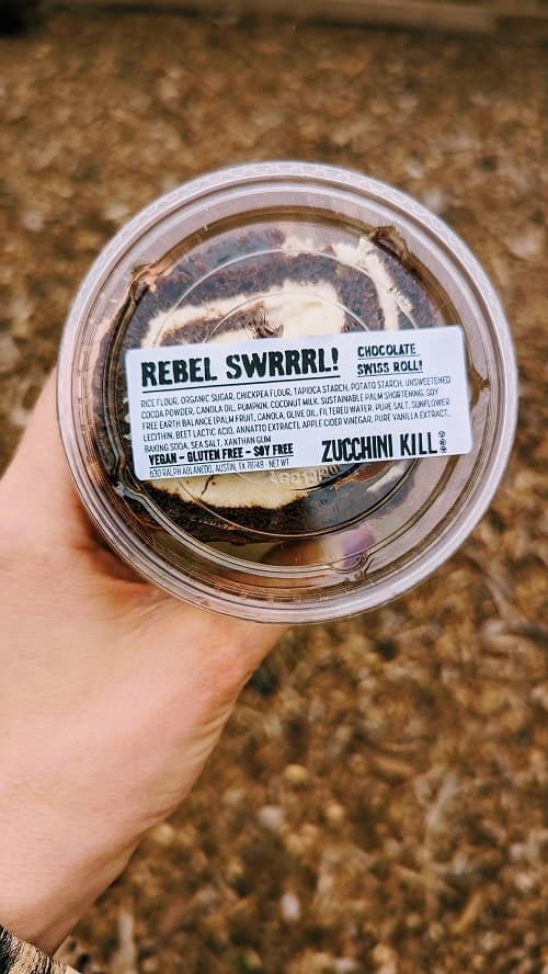 vegan chocolate swiss cake roll inside of a plastic container with a lid that says rebel swrrl from zucchini kill bakery in austin