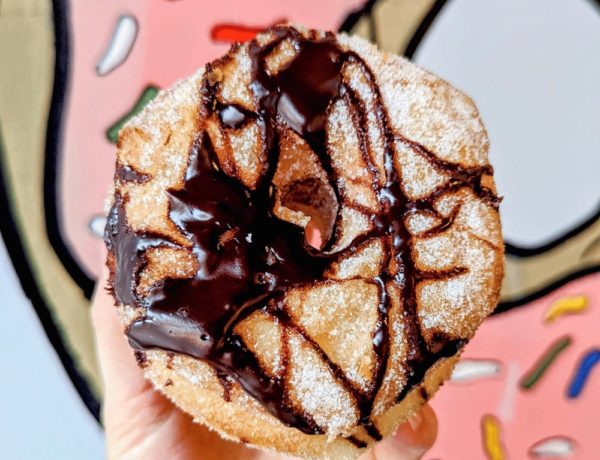 vegan cronut covered in a chocolate drizzle held in front of a pink donut background at machino donuts in toronto
