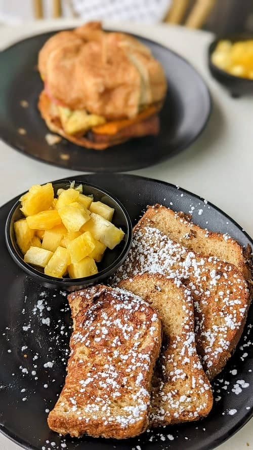 vegan french toast on a black plate in front of a croissant sandwich at rebel cheese in austin
