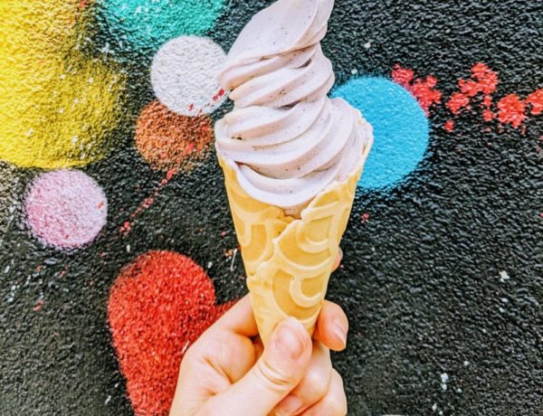 vegan lavender soft serve swirled in a waffle cone and held in front of a black wall with colorful circles at orchard grocer in NYC